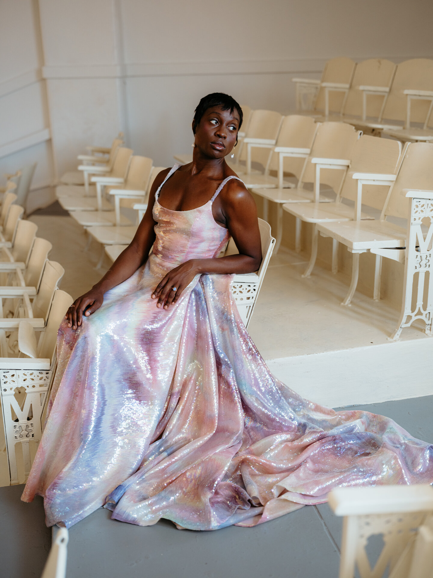 A model sitting on a chair wearing a rainbow beaded Loulette wedding dress.