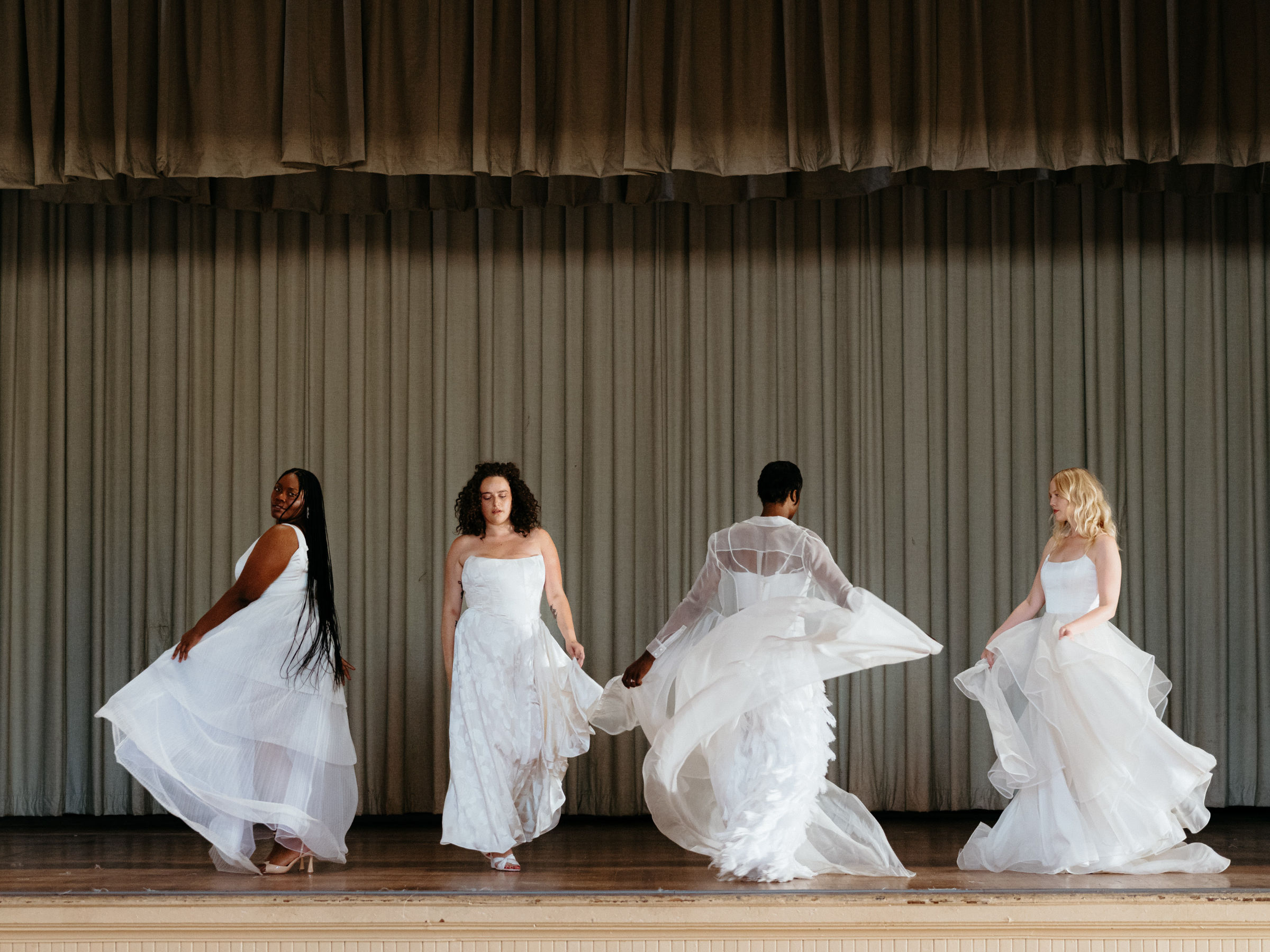 Four people on a stage wearing white wedding outfits from Loulette.