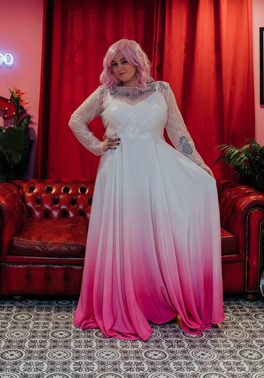 A model wearing a dip-dyed wedding gown with a white top and a gradient from white to pink on the bottom.