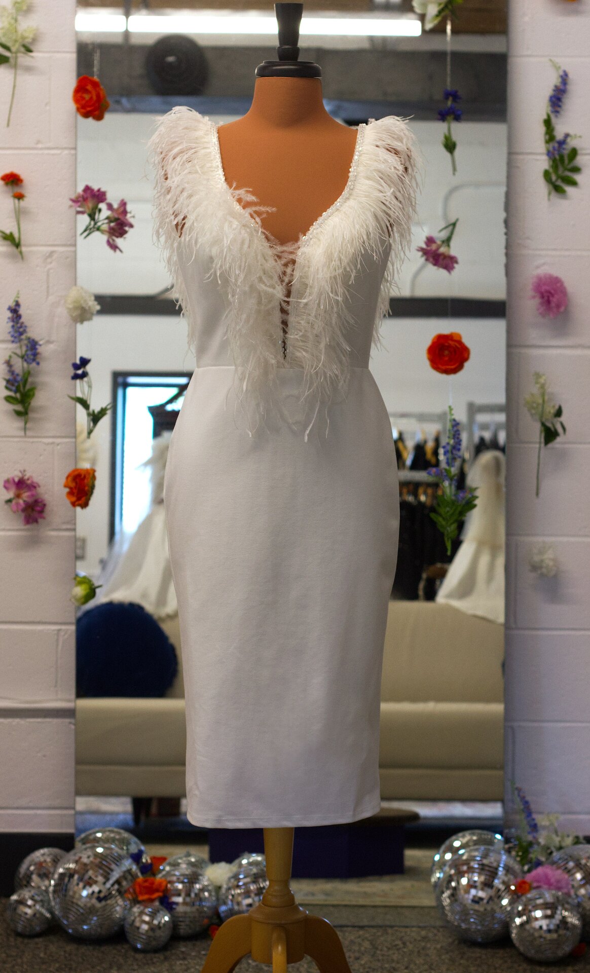 A white reception party dress with feather details on a mannequin.