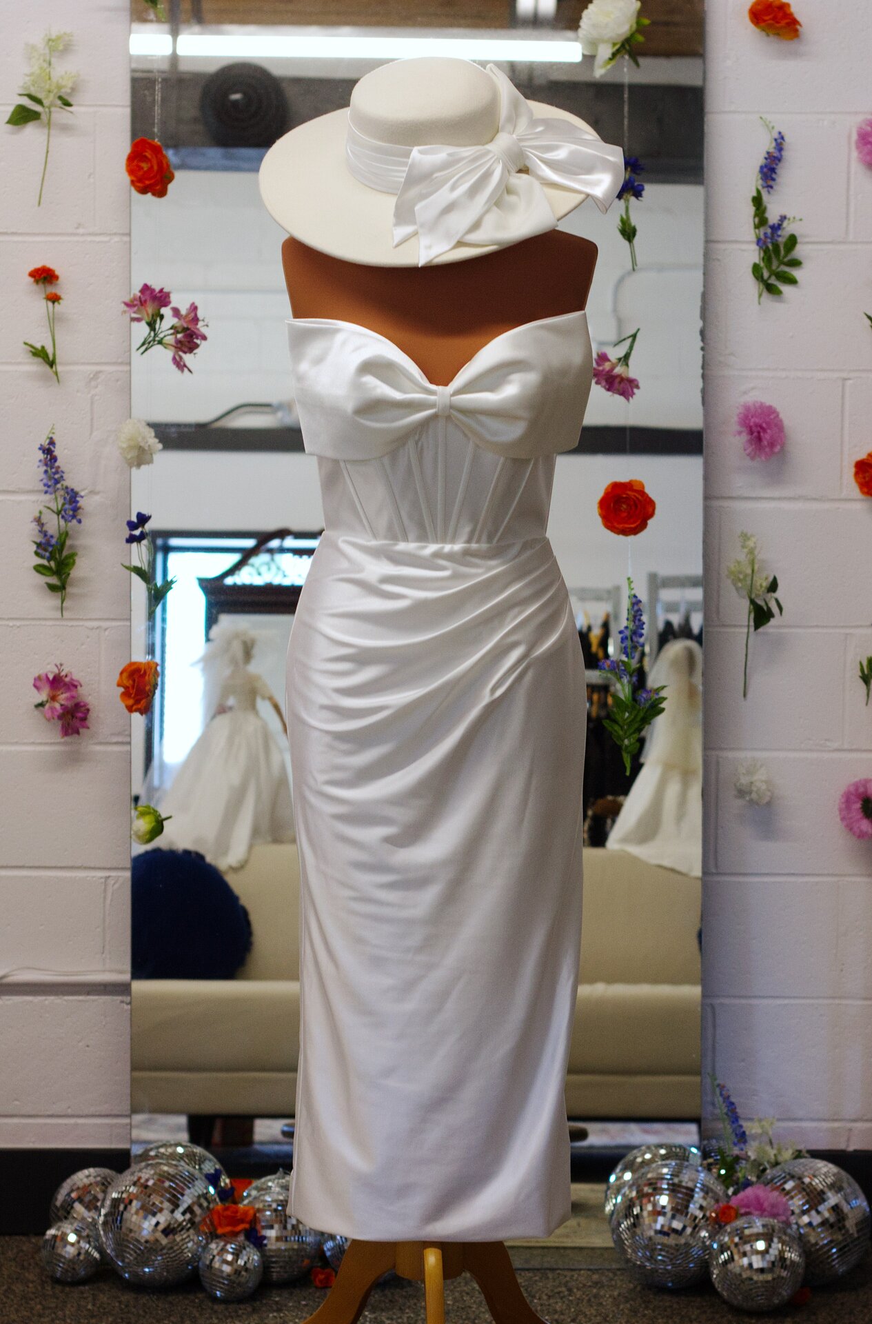A white tea-length reception dress with a big bow, paired with a bridal hat.