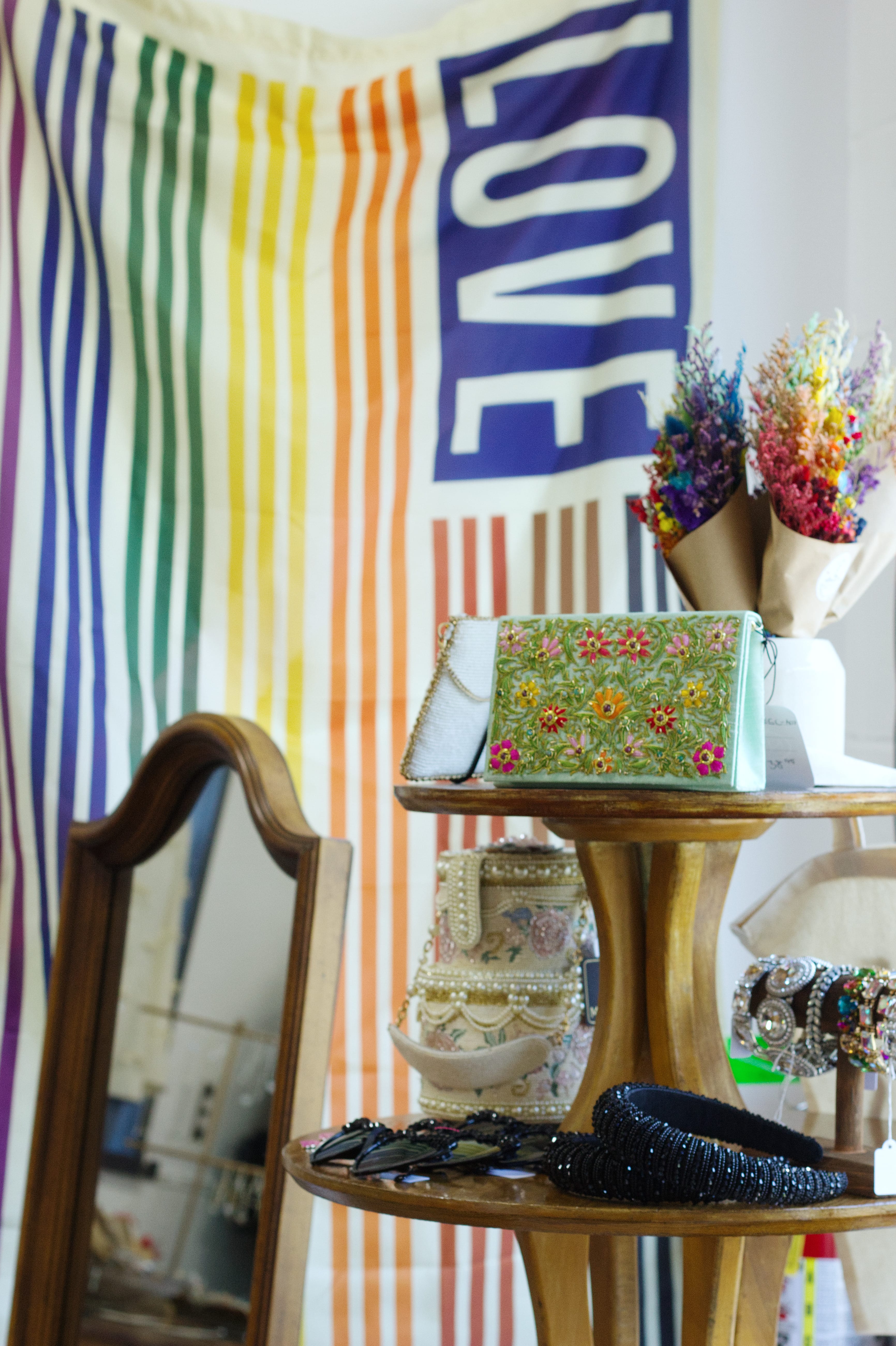 A display shelf with accessories including handbags, rainbow dried flower arrangements, and bracelets.