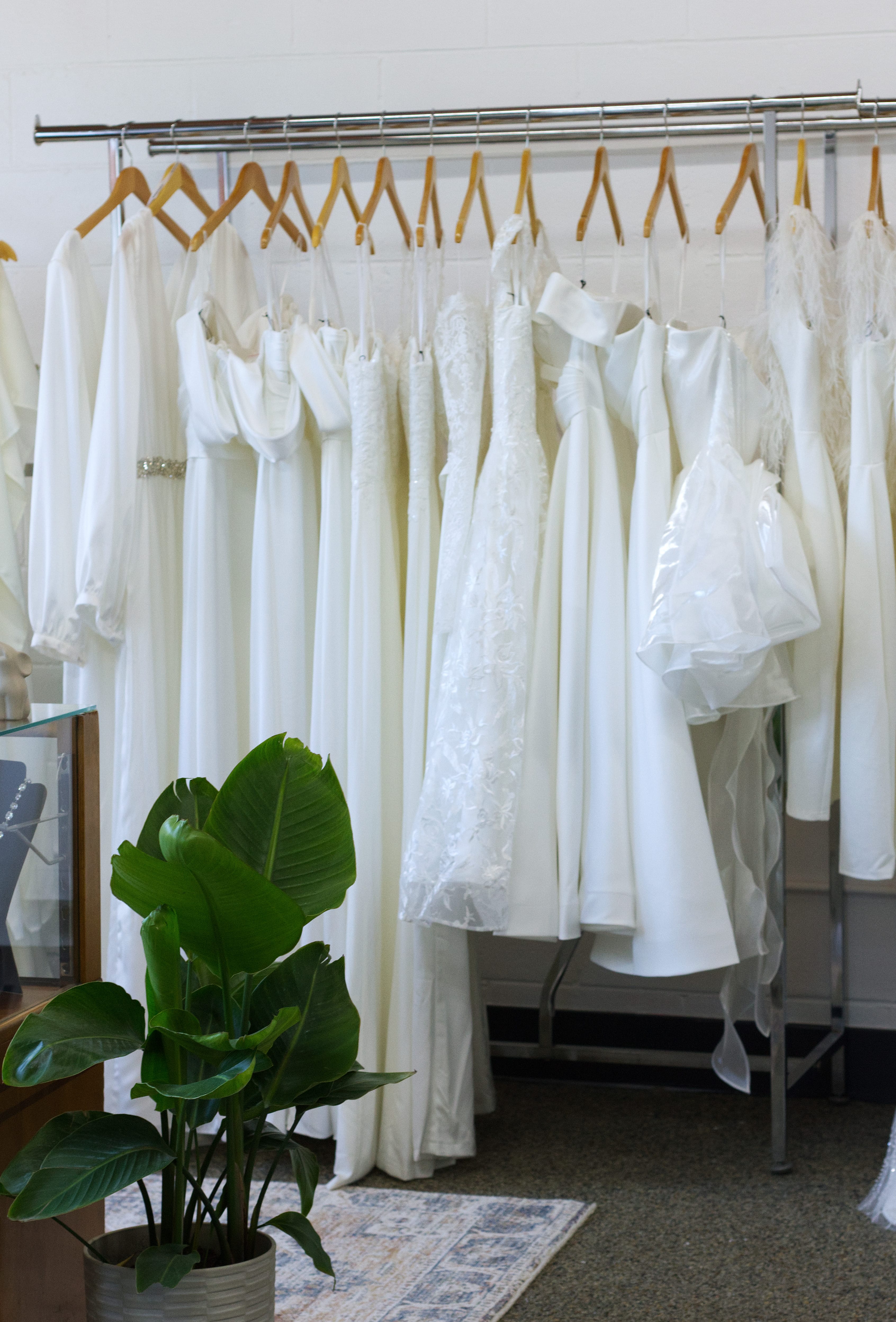 A rack of white bridal jumpsuits and short white wedding dresses.